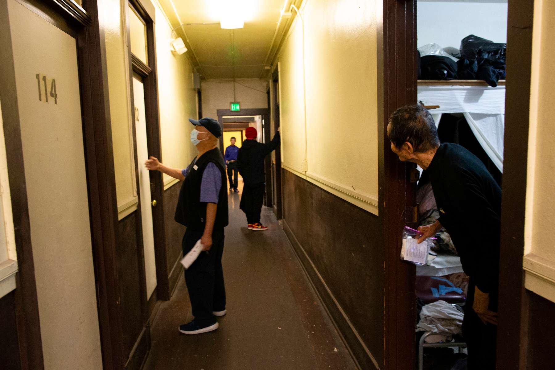 A resident in the Bing Kong Association building, a single room occupancy building, peers out from his door at the commotion in the hallway on April 21, 2020 in the Chinatown-International District in Seattle, WA. An employee from the Seattle Chinatown International District Preservation and Development Authority (SCIDpda) delivers masks to residents with the help from the building manager. Each bag contains three masks that were handmade and donated. 