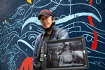 Photographer and co-founder of the International District Emergency Center (IDEC), Dean Wong, holdsa picture of Donnie Chin many years ago in the Chinatown - International District in Seattle, Washington on July 16 and 17, 2020. “He was Dragon one. I was Dragon two,” says Wong explaining that all the volunteers had a code name on the radio. Donnie Chin, director of the International District Emergency Center (IDEC) was murdered on July 23, 2015. The murderer was never found. The mural behind him was painted by Moses Sun and the Wing Luke Museum staff on the boards protecting the windows after the riots from the Black Lives Matter movement. (Photo by Karen Ducey)