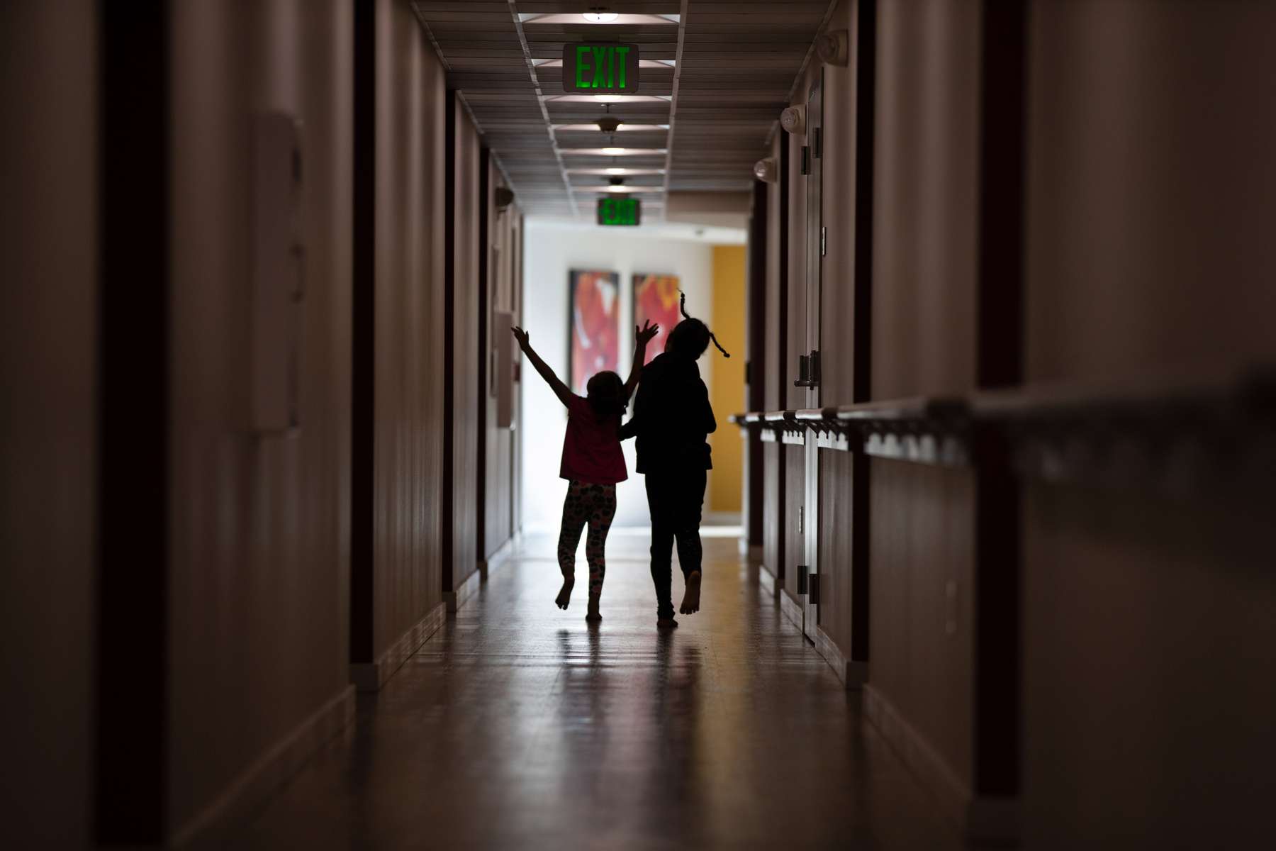 Sabrina, age 4, and Smira Sanura, age 6, run through the hallway of the Mercy House as their family remains in quarantine to help curb the spread of Covid-19 in Seattle, Wash. on October 21, 2020. They live with three other siblings including a newborn, two parents who work, and their grandmother in their apartment. One of the girls says the hardest thing about online learning is you have to mute and unmute yourself. She says this year has been difficult because sometimes other kids are allowed outside to play but their mother won’t let them. ICHS has a partnership with the Mercy House to pilot onsite health and wellness classes and events there. The girl’s mother, Amina Osman who works as a nurse says, “The biggest challenge is the fact that you have to be a mom and be a teacher at the same time. You have to multitask. Make sure food is at home and everything. So it's, it's been a tough taking care of a newborn and managing the kids as well.{quote} (photo by Karen Ducey)