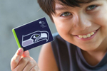 A child holds a Seattle Public Library card with a Seahawks logo on it at the Northgate Library in Seattle, Wash. on August 12, 2015. (photo Karen Ducey for the Seattle Public Library)
