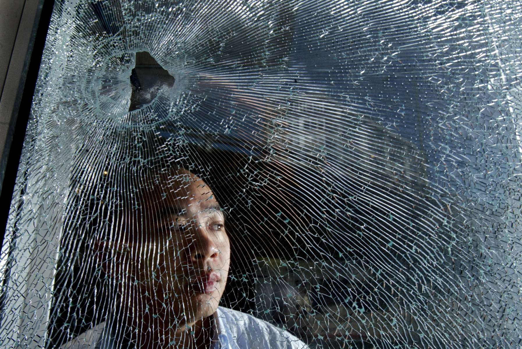 Henry Lo looks out the window of his business and home in Seattle.  A woman had been shot outside his doorway last night leaving a bullet hole in the front window of his office and blood on the sidewalk in front. (© Karen Ducey/Seattle PI)