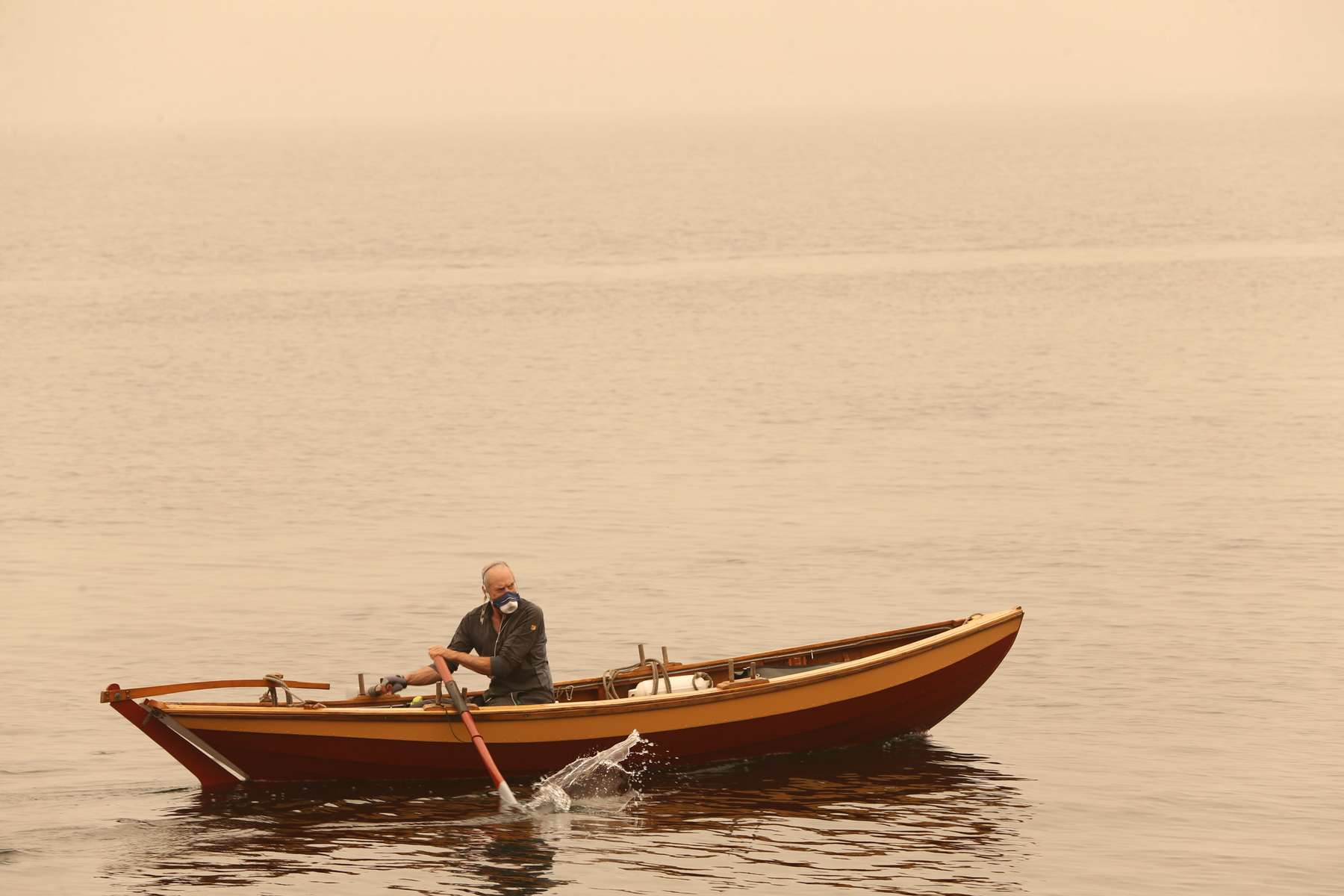 A man wearing a mask rows his boat as smoke from wildfires cover Seattle, Washington, U.S., September 12, 2020.  REUTERS/Karen Ducey