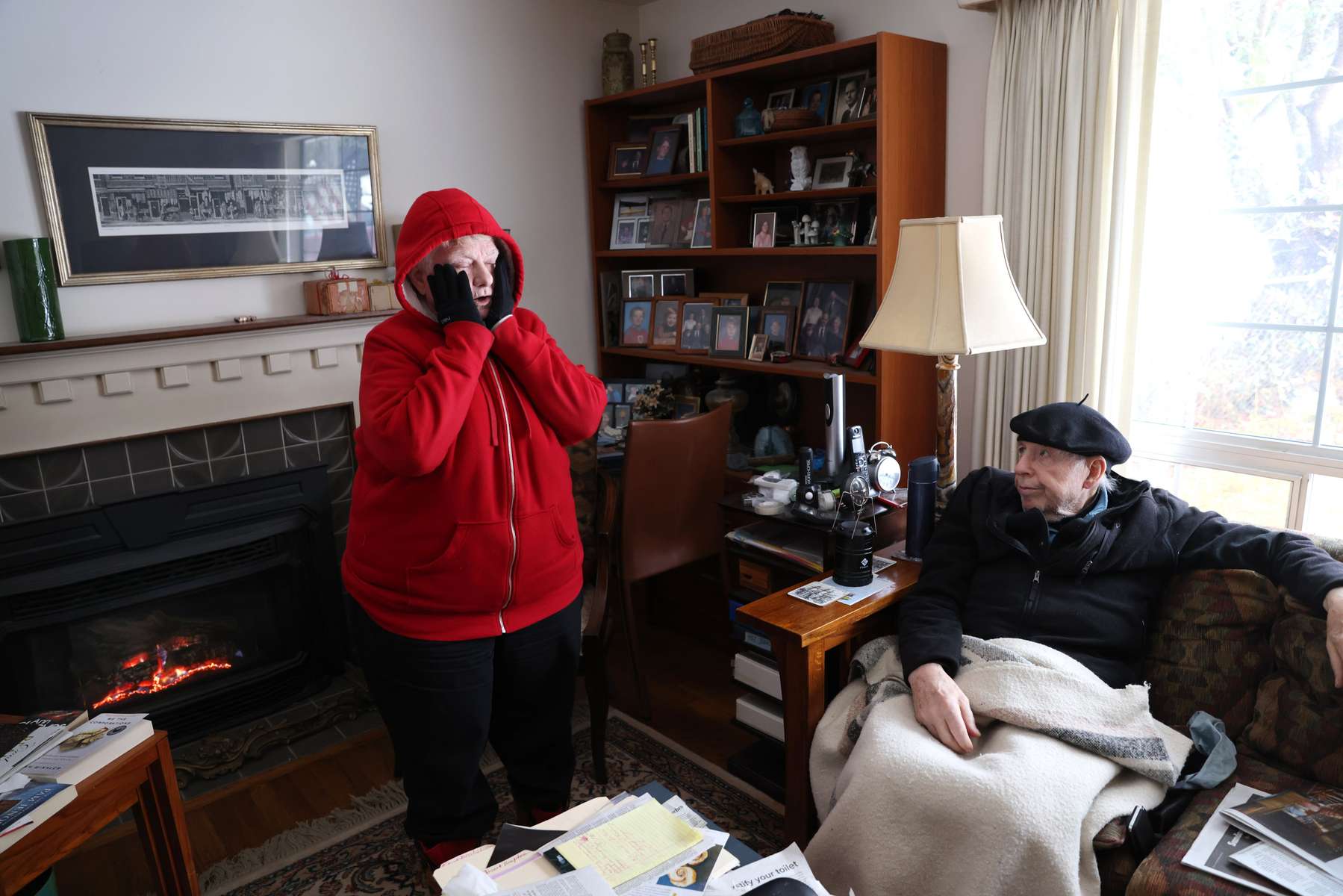 Nancy and Jim McMurrer try and stay warm by sitting by their gas fireplace under blankets in their home in Lake Forest Park on November 30, 2022. Their power, run by Seattle City Light, went out last night sometime before 10pm. “I kept waking up wondering what time it was,” said Nancy. They have several flashlights and lit candles throughout their house last night. Jim is thankful they at least have gas to run the fireplace -though the fan doesn’t run without electricity- and is concerned that so many cities are changing their building codes to not allow gas in new construction. The couple has hot water at least. Nancy says she is going to take a hot shower so she can feel “toasty and warm.”
