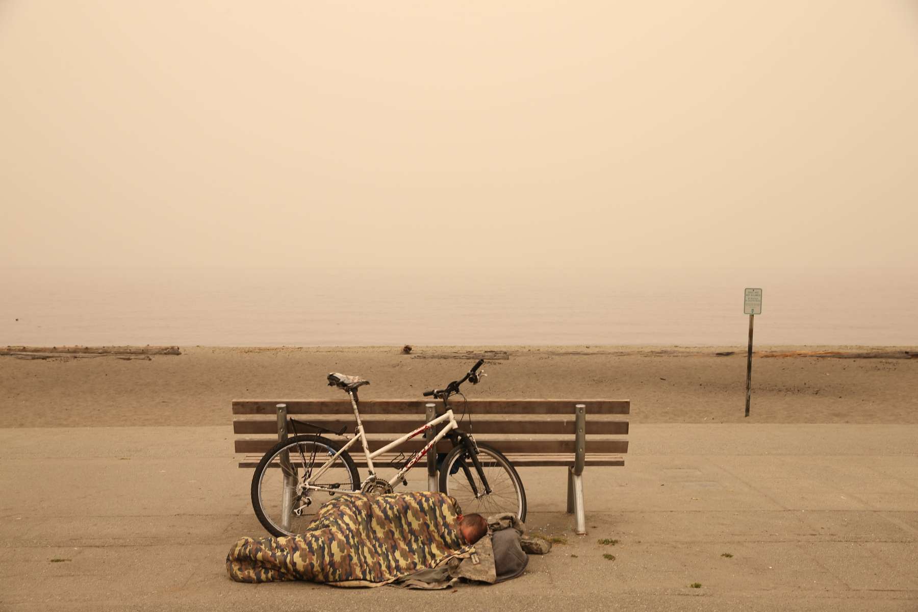 A man sleeps by a bench at Alki Beach in West Seattle as smoke from wildfires cover the city of Seattle, Washington, U.S., September 12, 2020.  REUTERS/Karen Ducey