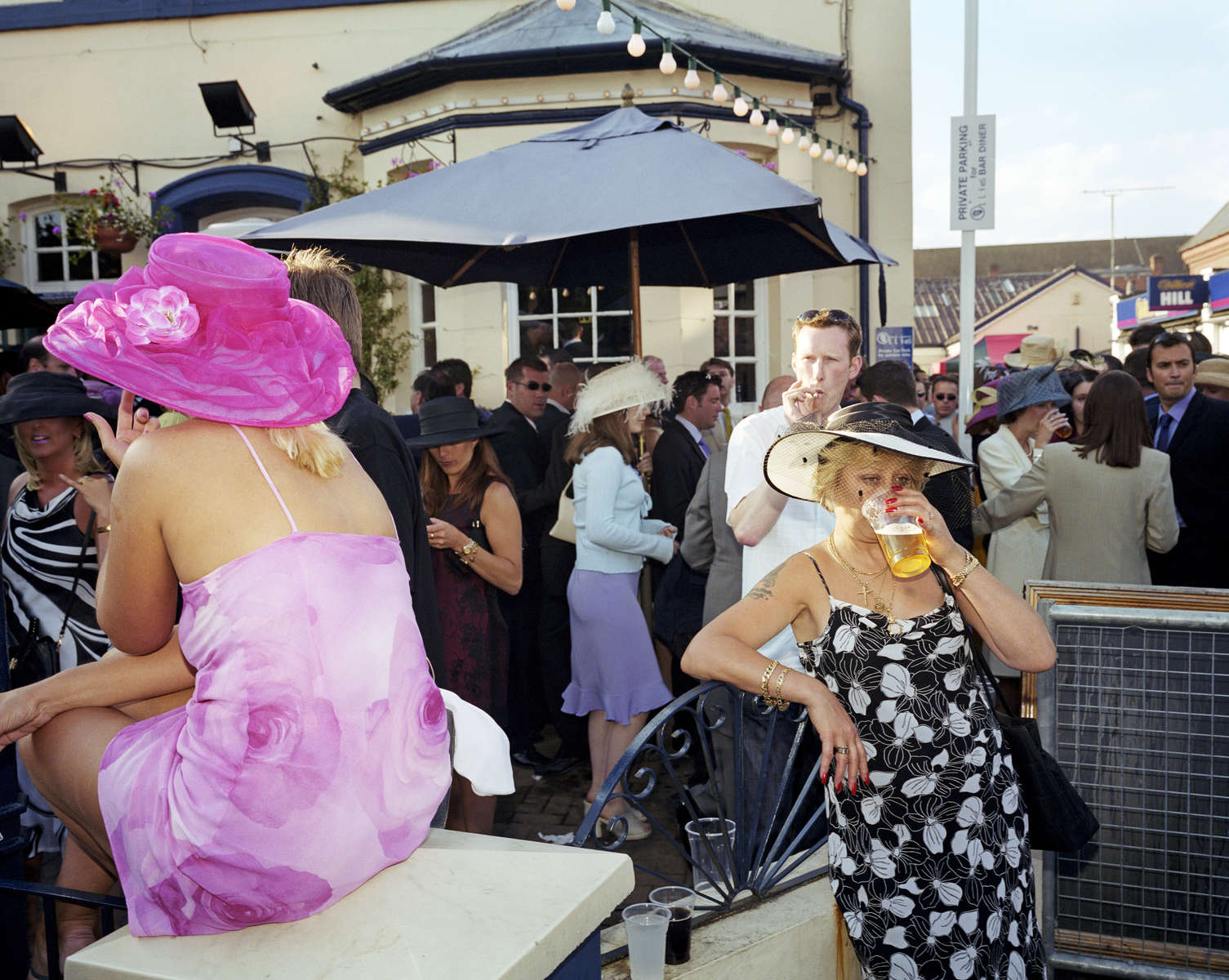 A woman dressed for Ladies Day drinks from a plastic pint glass outside a pub next to Royal Ascot Racecourse. June 2001