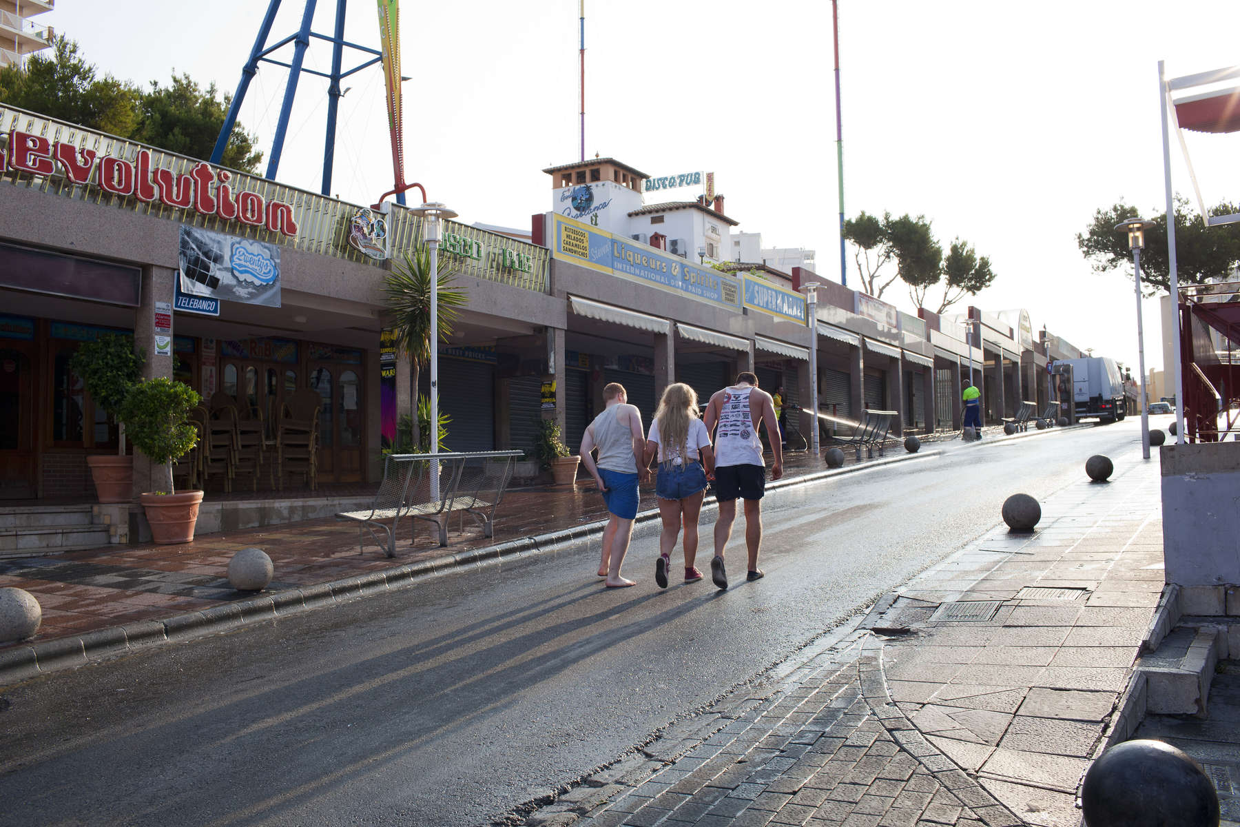 08:05 Three British friends make their way back to their accommodation as the sun rises over the main bar strip in Magaluf, Ibiza.