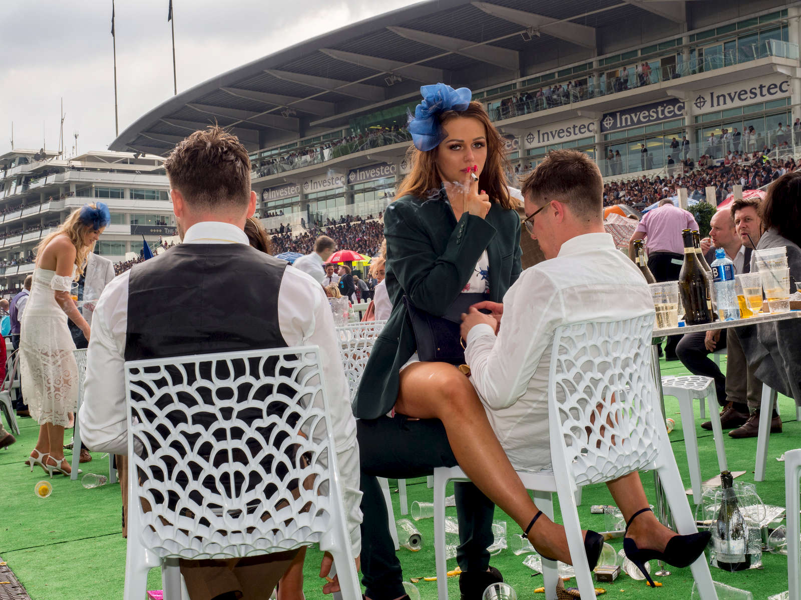 A young woman smokes a cigarette straddled across a man's lap on Ladies' Day at Epsom.Ladies' Day is traditionally held on the first Friday of June, a multitude of ladies and gents head to Epsom Downs Racecourse to experience a day full of high octane racing, music, glamour and fashion.