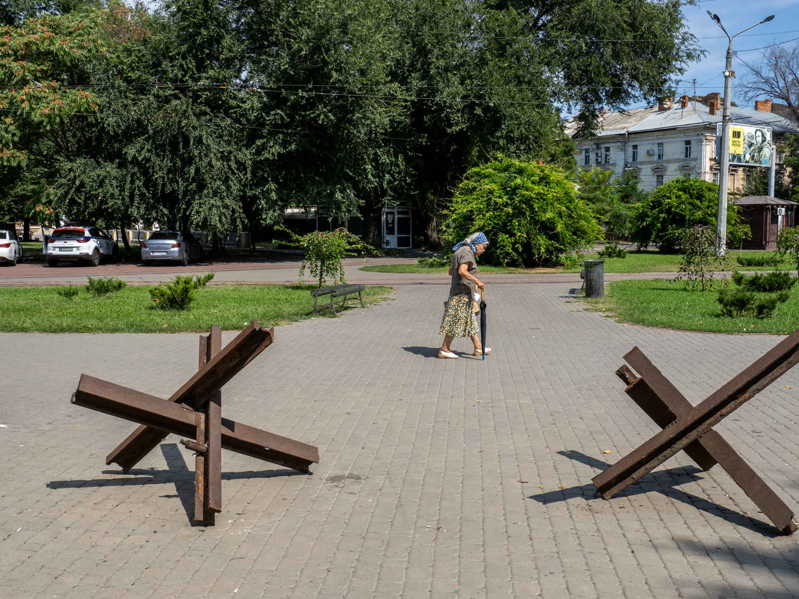 ODESSA, UKRAINE - AUGUST 26:  An elderly woman passes hedgehog anti-tank obstacles on the perimeter of Savytskyi Park near the railway station and District Court on August 26, 2023 in Odessa, Ukraine. (Photo by Peter Dench/Getty Images)