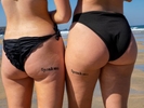 NEWQUAY, ENGLAND - AUGUST, 2022: Two women at Fistral Beach with matching Spank Me temporary tattoos. Temporary tattoos for visitors to Fistral Beach . During a heatwave in England, thousands of visitors headed to the town of Newquay, Cornwall for the surfing, beaches and Boardmasters Festival. Resources during the summer are stretched and some local residents are being pushed out of the area by tourists and due to an influx of holiday homes.