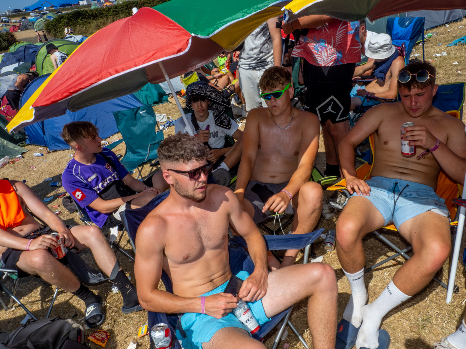 NEWQUAY, ENGLAND - AUGUST, 2022: Friends from Swansea, Wales realx in the shade at the Boardmasters FEstival camp site. During a heatwave in England, thousands of visitors headed to the town of Newquay, Cornwall for the surfing, beaches and Boardmasters Festival. Resources during the summer are stretched and some local residents are being pushed out of the area by tourists and due to an influx of holiday homes.
