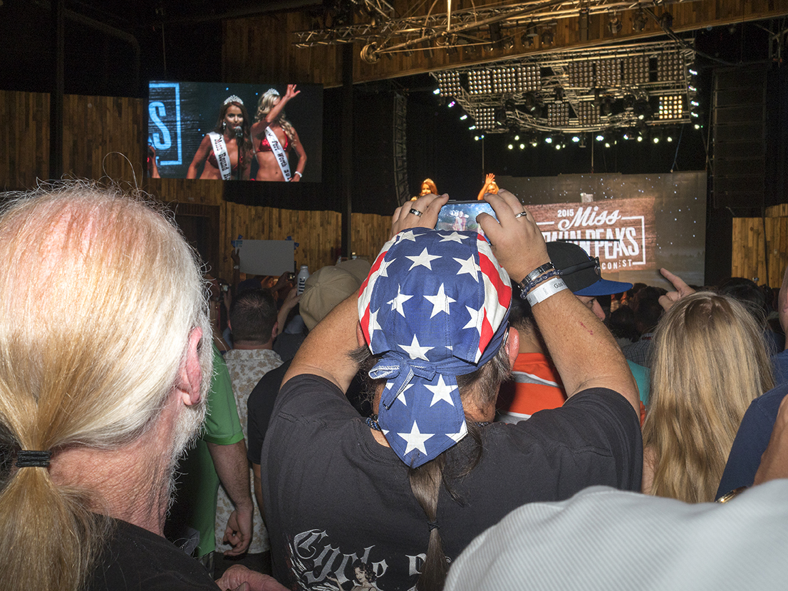 Supporters watch the finalists on stage at the Twin Peaks 2015 National Bikini Contest where around 68 girls from the USA competed for the crown for Miss Twin Peaks 2015, hosted at Gas Monkey Live Dallas, on the 24th June.Twin Peaks is a chain of sports bars and restaurants (colloquially referred to as breastaurants) based in Dallas, Texas. The chain is known for having its waitresses dress in revealing uniforms that consist of cleavage- and midriff-revealing red plaid (or sometimes black bikini) tops, as well as khaki short shorts. At other times, waitresses wear revealing seasonal or themed outfits. Restaurants are decorated in the theme of a wilderness lodge and serve a mix of American, Southwest and Southern cuisines as well as alcohol. The chain's slogan is {quote}Eats. Drinks. Scenic Views.{quote}Dallas is a major city in Texas and is the largest urban center of the fourth most populous metropolitan area in the United States. The city ranks ninth in the U.S. and third in Texas after Houston and San Antonio. The city's prominence arose from its historical importance as a center for the oil and cotton industries, and its position along numerous railroad lines.For two weeks in the summer of 2015, photographer Peter Dench visited Dallas to document the metroplex in his epic reportage, DENCH DOES DALLAS.Photographed using an Olympus E-M5 Mark II©Peter Dench/Getty Images Reportage