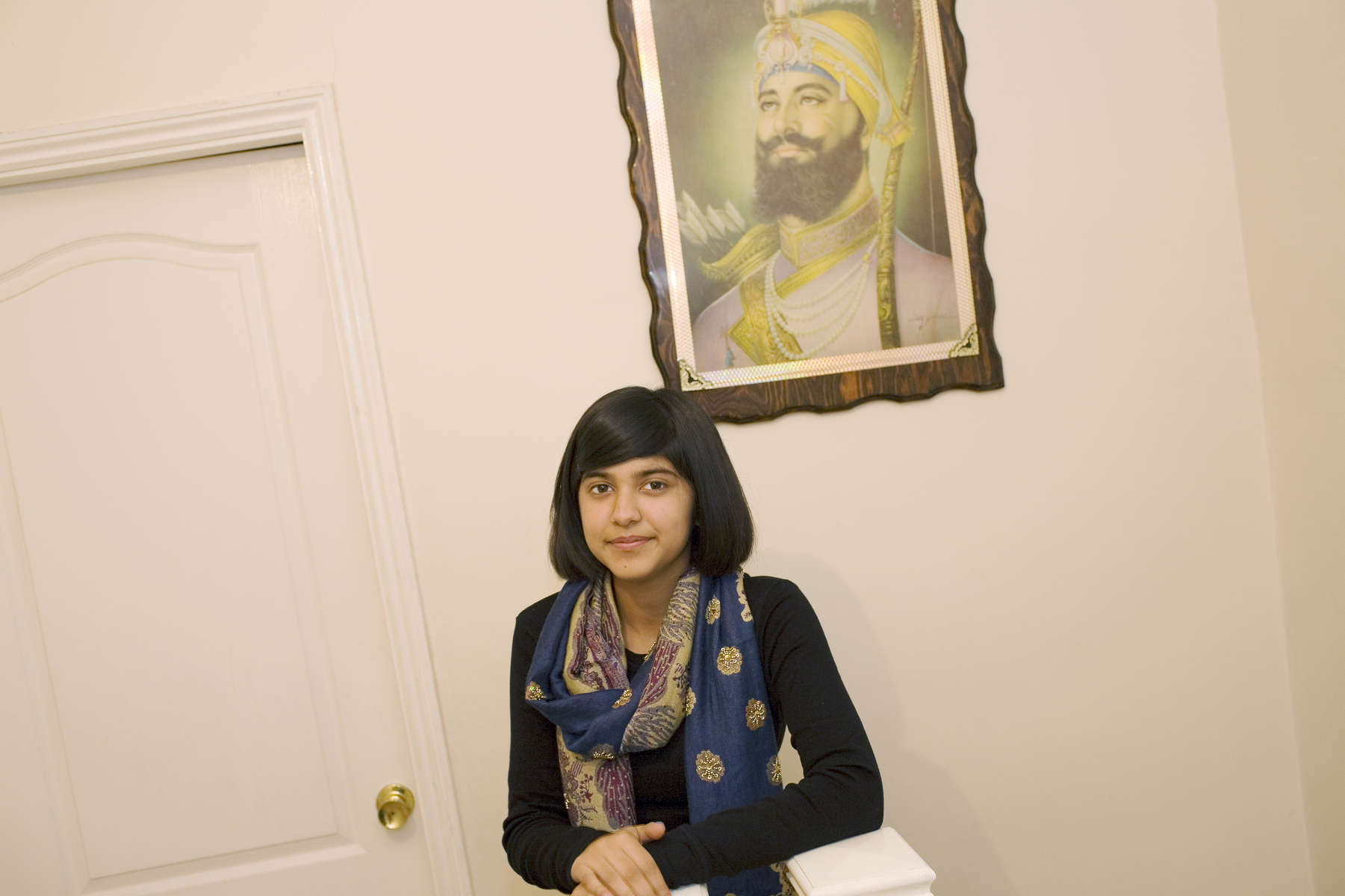 15 year old Robyn Kullar under a portrait of Sri Guru Gobind Singh at her home in Southall where she lives with her mother Sarbjeet (40), grandmother Kuldeep (59) and sister Alisha (13). Her family are Sikh but Robyn admits to being an Atheist. She enjoys the cultural aspects of Sikhism and will celebrate various festivals including Diwali.  Robyn is a pupil at Villiers High School.Villiers High School is in the town of Southall. It has a very wide ethnic diversity. 45 different 1st spoken languages are listed among the 1208 pupils. 25 ethnic groups are represented with Indian, Pakistani and Black-Somali the three highest.Southall is a suburban district of West London, England. The town has one of the largest concentrations of South Asian people outside of the Indian sub-continent. Over 55% os Southall's population of 70,000 is Indian/Pakistani, with less than 10% being White British.
