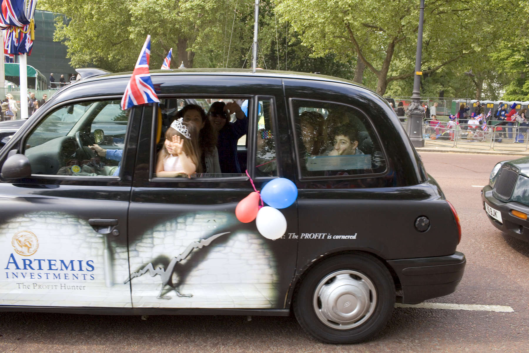 A young girl wearing a tiara waves from a black London taxi on the Mall heading towards Buckingham Palace.