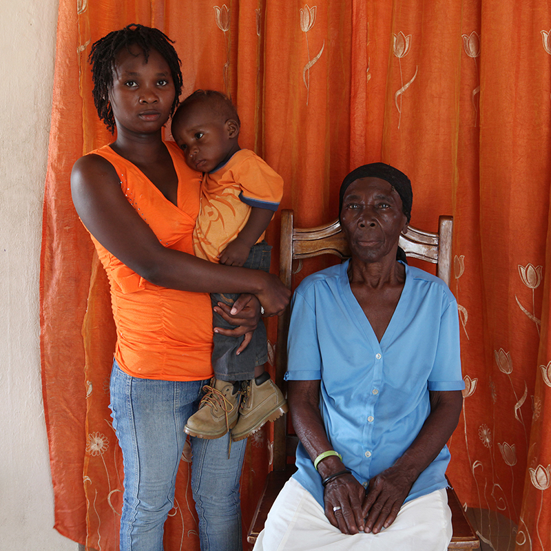 Amania Dèrrile, 60 years oldBorn in the city of Petit Goave, she now lives in Port-au-Prince in Cite Soleil.She has ten children. Here she is shown with her granddaughter Widline and her great-grandson who she helps take care of.