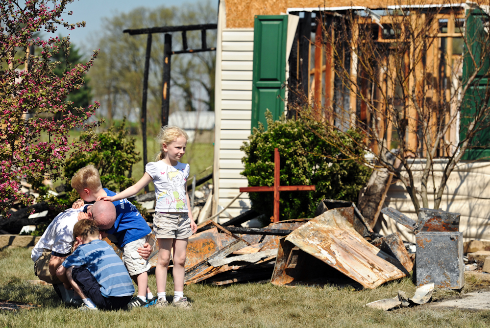 Gabe Lambert grieves the loss of his grandfather, with his children, Luka, 8, front, Anson, 6, back, and Mya, 7, right, at the site of house fire at 738 Strawberry Hill Road in Evansville on Wednesday, March 21, 2012.  Donald R. Lambert, 81, perished in the fire that destroyed his home and his neighbor's home and damaged several others in the neighborhood.  Lambert's son, Greg, not pictured, made and placed a cross to honor his father in front of the destroyed home.