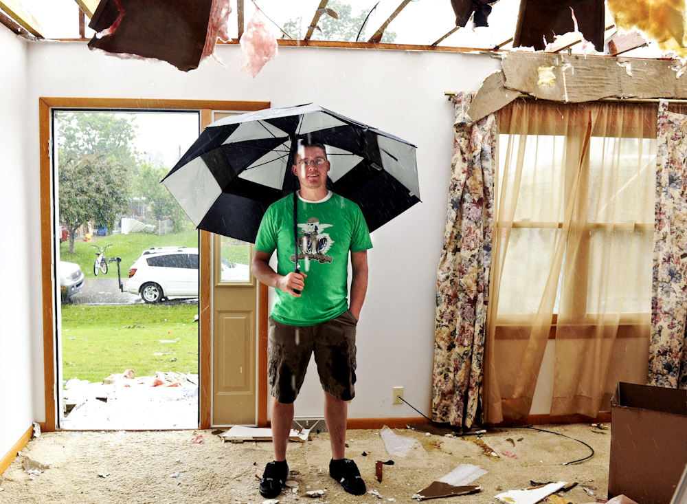 Wes Mofield tries to stay dry as he stands in his grandmother's living room at 106 S. Weber Drive in Haubstadt, Ind. Family members believe a tornado hit the home when a line of severe storms blew through the area the night before. 