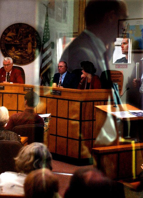 Local citizens waiting in an over flow area are reflected in a door window at the entrance to the Indian River County Commission chambers at the County Administration Building in Vero Beach on Tuesday, December 14, 2004.  The commission held a public hearing on a proposed moratorium that would delay rezonings and site plan approval for new residential areas.  Indian River County Sheriff's deputy, Christian Mathisen, top right, monitored the chamber, which was at capacity.