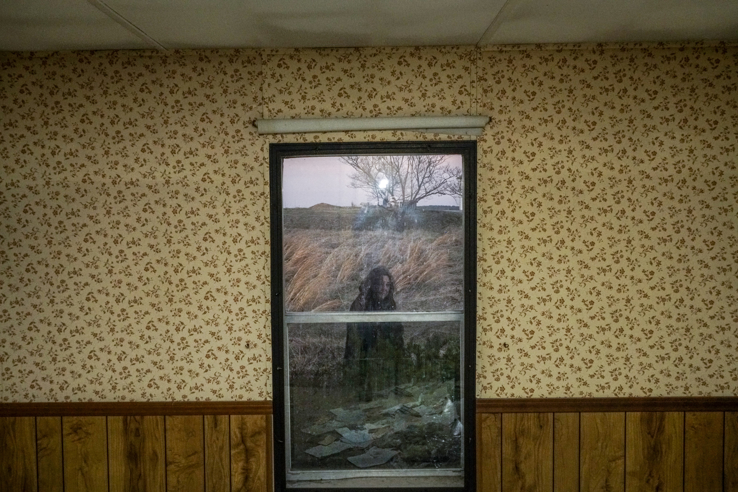 2017. Illinois. USA.  Georgia de la Garza, a local environmental access in Southern Illinois.  She is pictured from inside an abandoned house near the Eagle River Coal Mines-Franks LLC in Harrisburg, Illinois.  Mining jobs have been the core of the economy in Southern Illinois for the past century, a source of stability, prosperity and pride. In the last few decades the number of jobs have declined to a small fraction of their former number, leaving the economy in shambles with few prospects for new forms of industry to take its place.