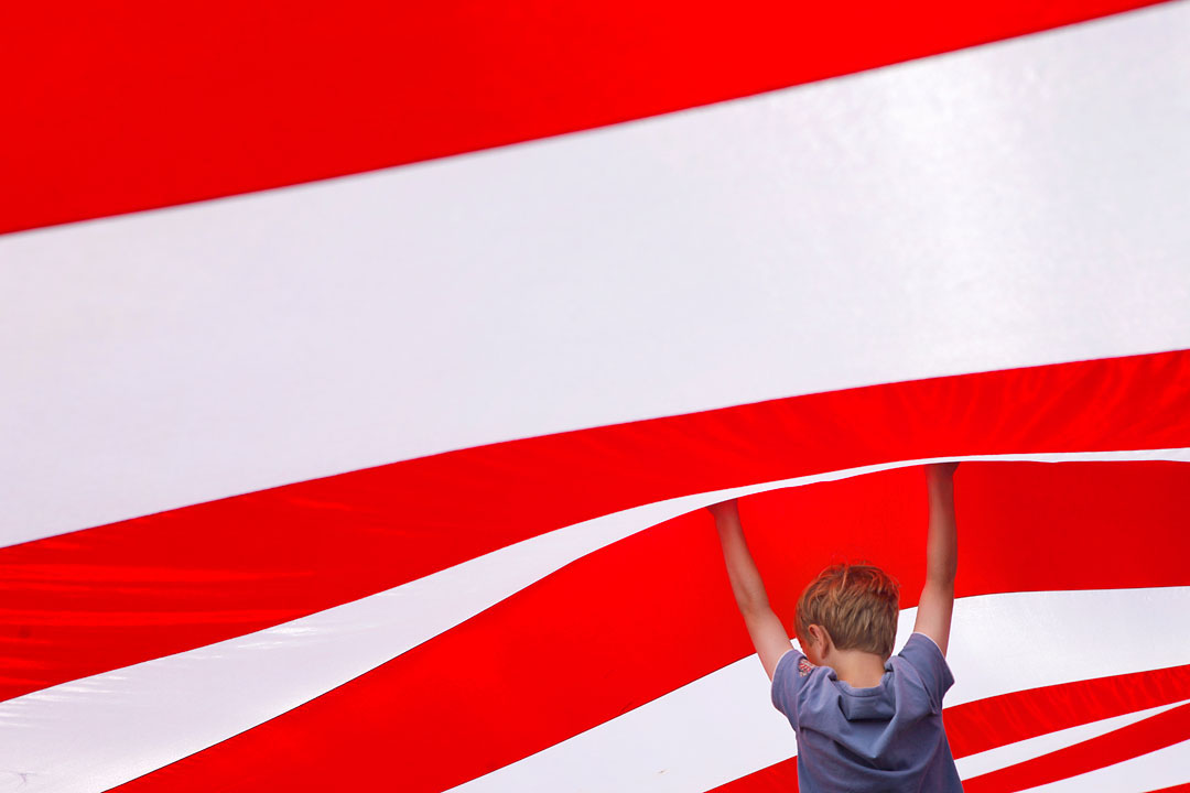 Eamon Malley, 7, of Salinas tries to hold up the large American flag covering the arena grounds at Sunday's California Rodeo Salinas.