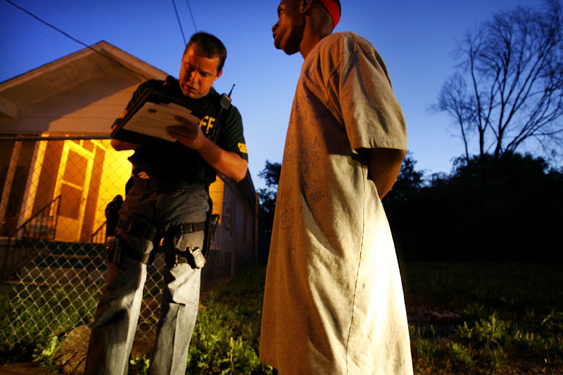 A Shelby County deputy with the Street Crimes Unit takes notes while talking to a suspected Blood in the Hyde Park area of North Memphis. His brother was shot more than a dozen times in a gang hit. The young man is wearing a shirt covered in gang symbols to memorialize his brother. The murder remains unsolved. (Mike Brown/ Memphis Commercial Appeal)