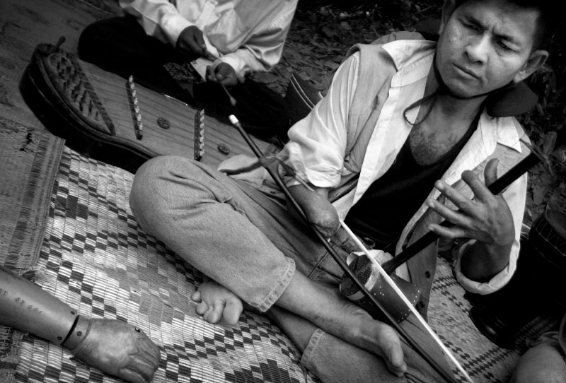 A musician performs in the Cambodian jungle outside the Banteay Srey Temple. This man who lost his vision and forearm from a land mine explosion now plays music with the Angkor Association for the Disabled.  He accepts donations from tourists instead of begging on the streets within the city.(© Mike Brown)