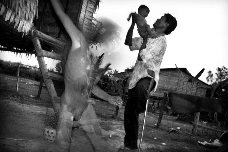 Jen Kina tosses his 5 month-old unnamed son in the air as his 7 year-old son Peap plays in front of the family's home in Kamtrork Village. With a little help from the international community there is hope for young Peap to break the cycle of impoverishment in the country and regain a rich cultural heritage.(© Mike Brown)