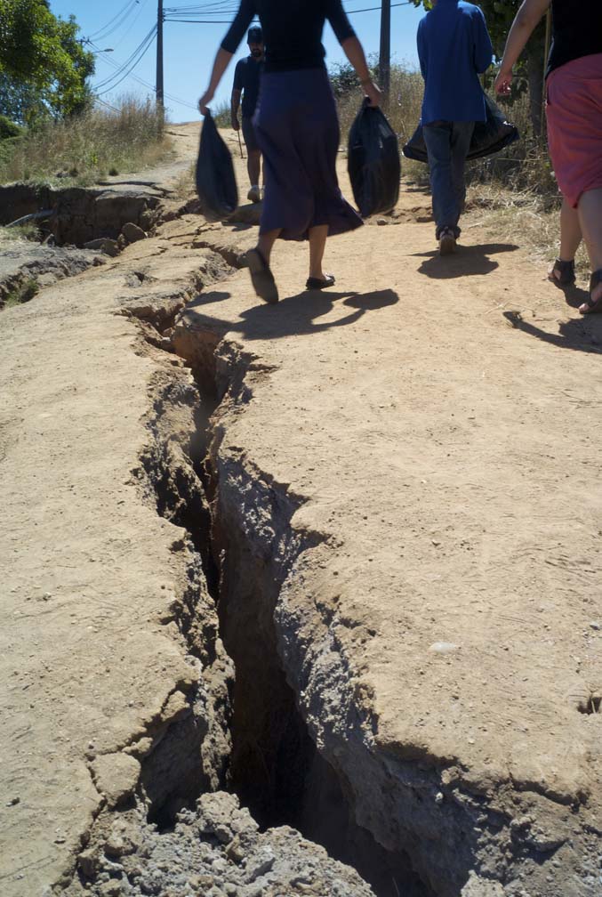 A massive crack in the ground is visible as several people walk carrying bags filled with supplies.