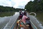 An Afro-Ecuadorian man operates a small motor-powered boat while another removes water that has leaked into the boat, as a female passenger sits quietly.