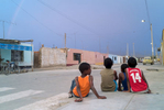 Four young Afro-Peruvian boys are sitting on a curb, on an empty street, observing a rainbow.