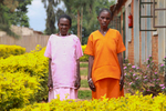 This is a portrait that features two Rwandan women (65 and 85 years old), wearing different colored prison uniforms, standing outside (side-by-side) and looking into the camera.