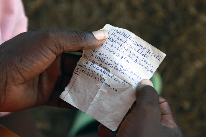 It's a tight shot showing the hands of an inmate holding a small sheet of paper; visible are the names of the ten people the inmate killed during the 1994 genocide.