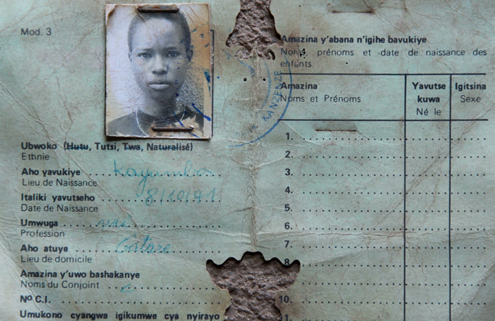 A badly worn Rwandan national identity card is photographed on the ground; the card lists the owner as Tutsis and includes her photograph.