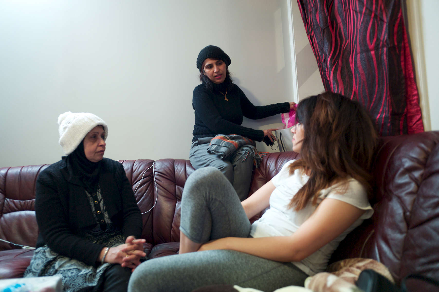 Rejected asylum seeker removes her belongings from behind sofa while seated with two friends.