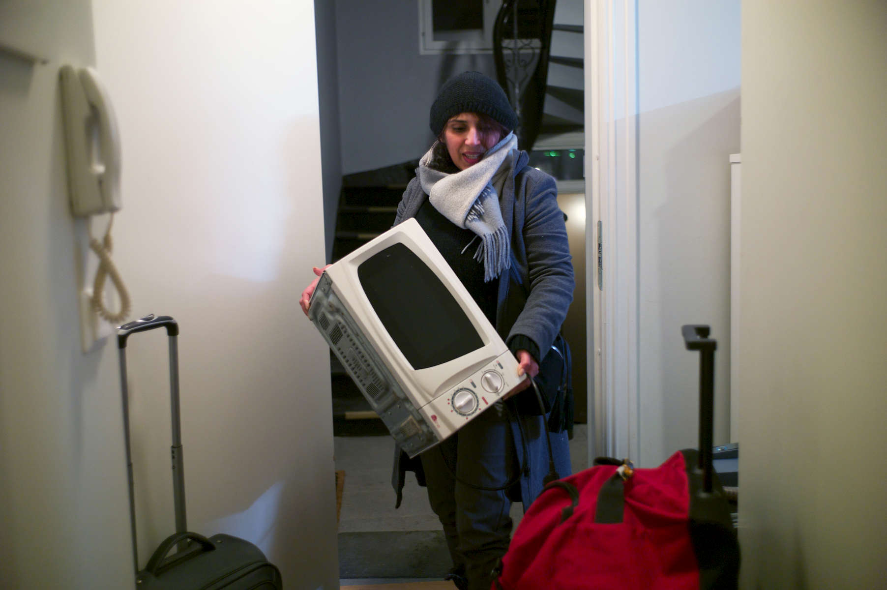 Rejected asylum seeker enters apartment doorway carrying a microwave oven.