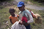 Two young Afro-Bolivian girls, one with a white doll strapped to her back, walk home carrying a sheet filled with oranges.