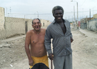 Two Peruvians, one black, flashing smiles and standing on a desolate street, pose for a photograph as one jokingly elbows the other in the side of the body.