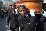 An Afro-Peruvian man, with a casket resting on his shoulder, answers his cellphone during a funeral procession.
