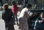 Two middle-aged Argentinian women give religious pamphlets to two homeless men (one sitting the other standing) outside a church.