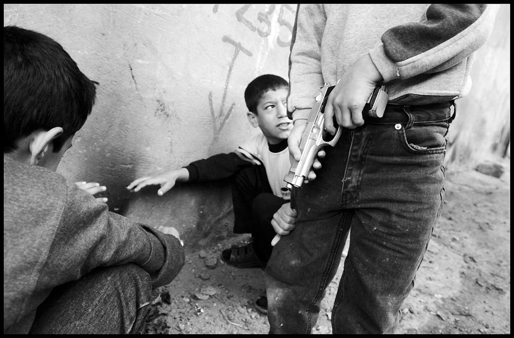 Eleven year-old Suleyman Semsiya grabs the pant leg of his friend Kadir Aktas who holds a toy gun. The chidlren warm themselves in an alley with their friend Recep Uran.  {quote}Of course we'll have real guns when we grow up..{quote} Kadir says, {quote}...in case there is a fight.{quote}