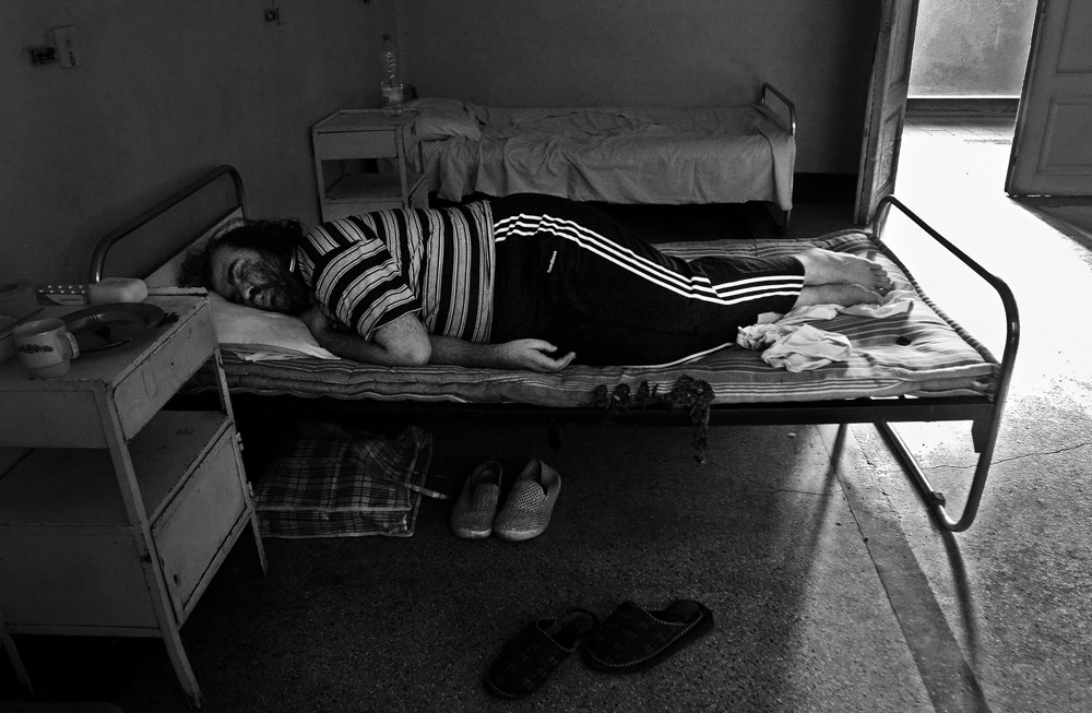 A patient sleeps in a room that can accommodate six occupants of both genders in a psychiatry ward of a county hospital in Bulgaria, on August 03, 2006. He says the mattress underneath him is at least ten years old, and he complains it is difficult to sleep on it because it is ”infested with fleas.” All of his belongings -- including clothes, shoes, food utensils and bed sheets -- he brought from home because the hospital could not provide any of them. 