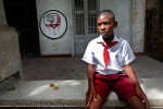 A young student wearing the uniform of communist youth rests in front of an office for the CDR (Comité de Defensa de la Revolución, or Committee for the Defense of the Revolution,) which is a network of neighborhood watch organizations reporting on any {quote}counter-revolutionary{quote} or anti-communist activity, in Havana, Cuba. My grandfather spent 5 years of his youth in a labor camp for political dissidents after one such neighborhood watch organization noted his lack of participation in the communist party - thus labeling him a person of conflict with the government of Bulgaria.  Elementary schoolchildren wear pañoletas, or scarves as part of the uniform of the José Martí Pioneer Organization for children operated by the communist party - that is quite similar to a communist youth organization in which I had to partake as a young Bulgarian student - blue or red in color depending on their age, and switch to yellow and white uniforms in adolescence.  