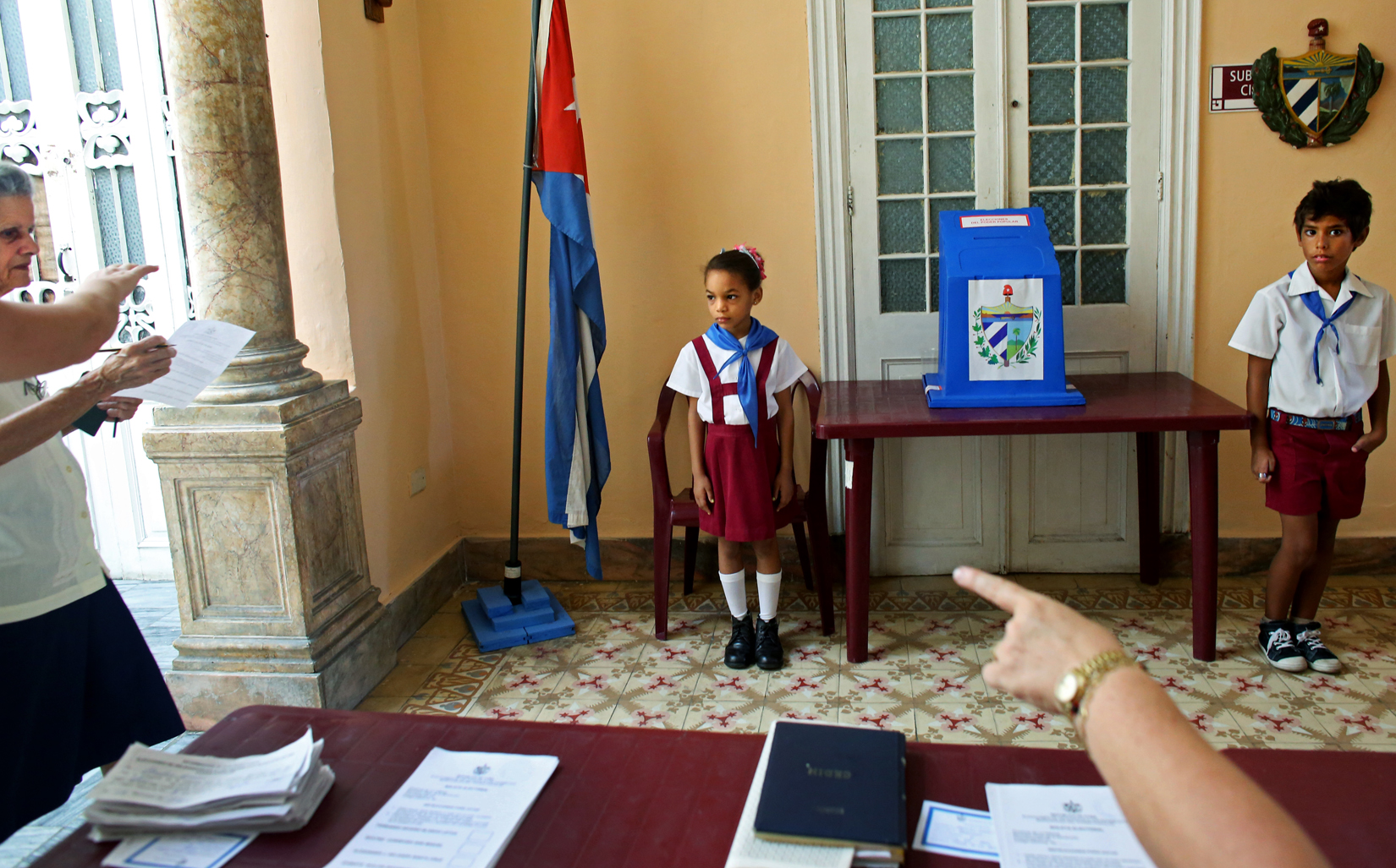 Children wearing the uniform of communist youth are directed to salute {quote}Votó!{quote} ({quote}S/he voted!{quote}) as a woman places her ballot in Cuba's Elecciones Parciales (Partial Elections) to elect delegates to the Municipal Assemblies of People’s Power, the country's unicameral parliament, on April 19, 2015 in Havana, Cuba. The delegates function as district representatives for a 2.5 year term.Little Pioneers - members of the José Martí Pioneer Organization for children operated by the communist party - are often sent by polling station presidents to people's homes as a means to motivate citizens to the polls. (Voting is not mandatory, but frowned upon if not exercised.) Kids usually enter the organization in elementary school, wearing blue or red scarves - or pañoletas - to indicate the student's level, and continue until adolescence, switching to yellow and white uniforms in high school. 