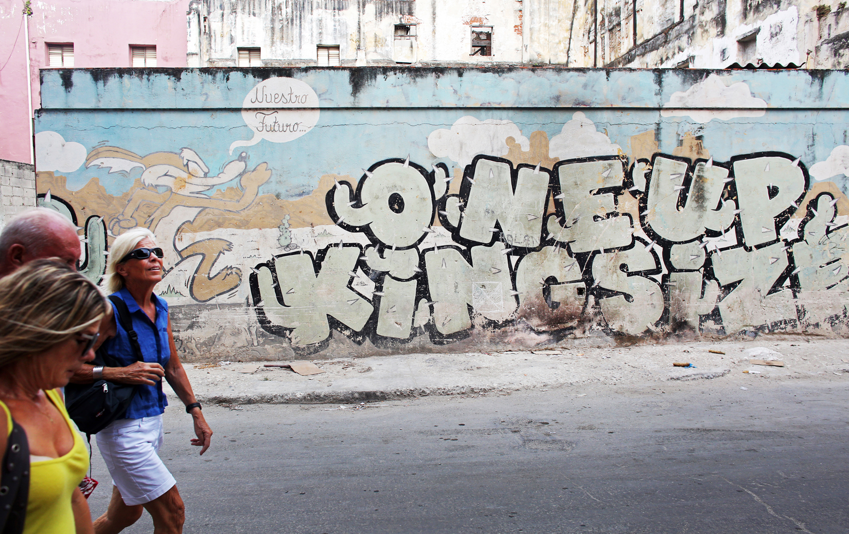 Tourists walk by graffiti of the American cartoon character Wile E. Coyote and his speech bubble {quote}Nuestro Futuro (Our Future,){quote} running by a cactus shaped to read {quote}One Up King Size,{quote} in the Havana Vieja neighborhood of Havana, Cuba. It is said to reflect the fear that a further thawing of U.S.-Cuban relations will permanently alter the cultural and economic make-up of the island. In the cartoons, Coyote repeatedly and unsuccessfully attempts to catch a fast-running ground bird, The Road Runner, his plans for capture always backfiring in injury. 