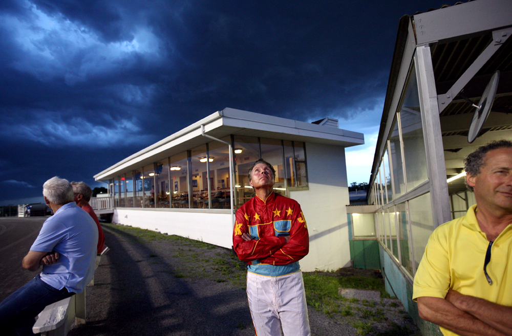 Joe Kowalski (center) checks the darkening clouds during a horse race at the Yonkers Raceway in Yonkers, New York on Tuesday, May 29, 2012.(For The New York Times)