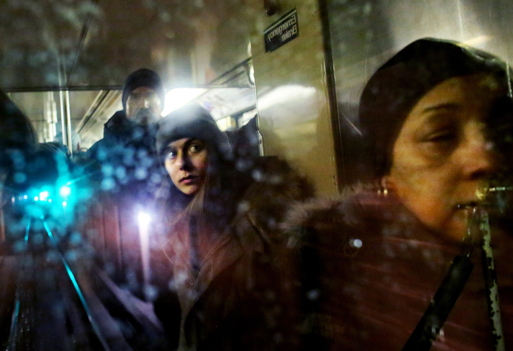 Aude Back de Surany, center, and other passengers are reflected in the back window of an uptown C train traveling through a subway tunnel in New York, New York on January 30, 2015. (For The New York Times)