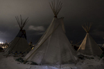 Teepees illuminated by the floodlights of the ongoing DAPL pipeline construction in the background.