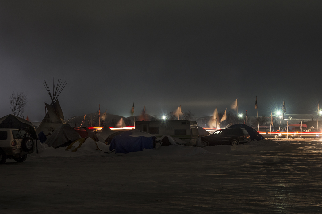 DAPL floodlights shine in the background as traffic continues into the night on Flag Road at the Oceti Sakowin camp at Standing Rock.