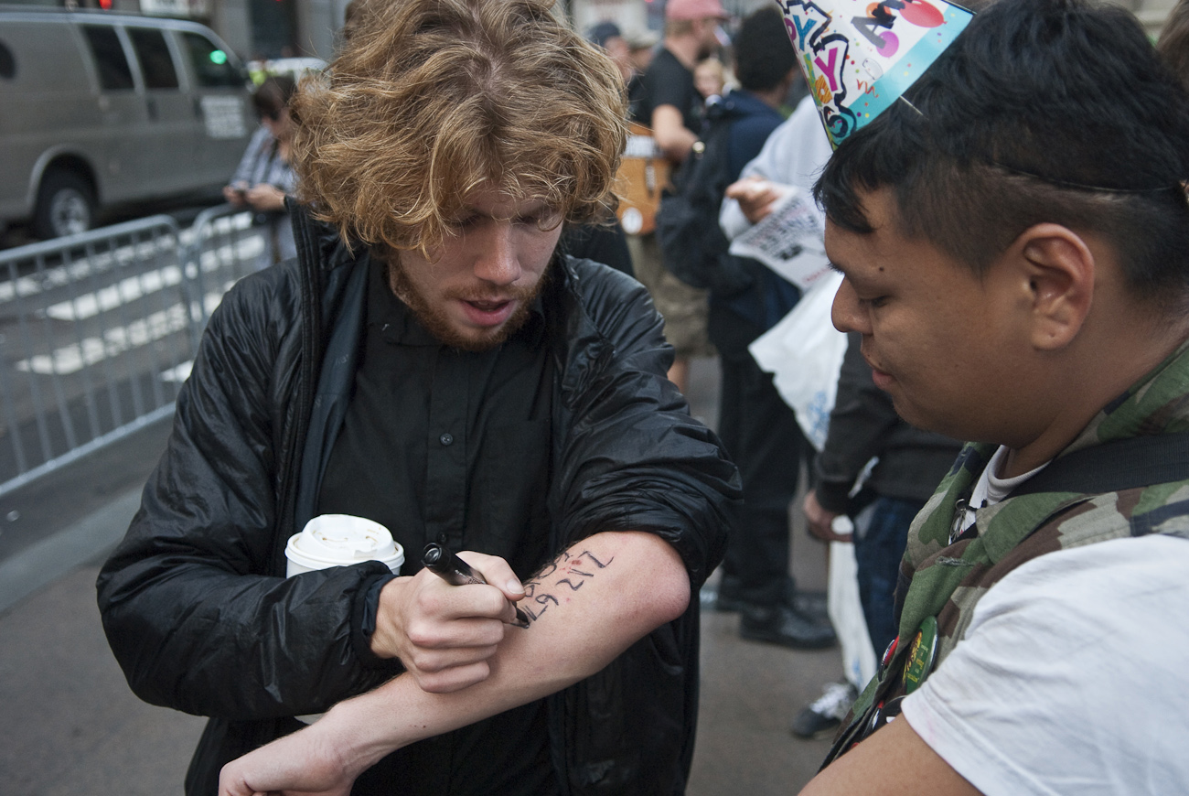 A young man uses a marker to write down the number of the National Lawyers Guild Hotline. The Guild provides lawyers and jail support to anyone arrested during these demonstrations. When asked the NLG also provides trained {quote}Legal Observers{quote} to monitor police and civil rights abuses during large gatherings, planned actions, and demonstrations such as took place on September 17th.