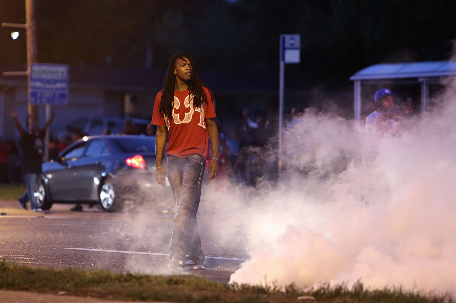 A man stare defiantly at police was he walks through a cloud of tear police deployed to dispersed a crowd at the corner of Lang Drive and W. Florissant Avenue on in Ferguson, Mo. Monday Aug. 11, 2014. 