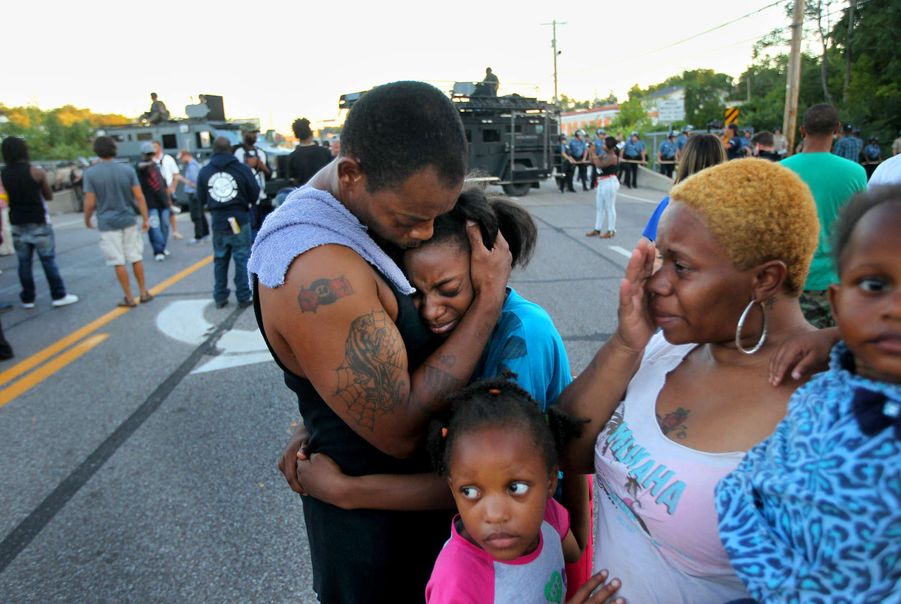 Terrell Williams El, comforts his daughter Sharell Williams, 9, as Temika Williams, 6, (bottom) stays close to her mom Shamika Williams, and sister Shanell Williams, 2, near a line of police in riot gear on West Florissant Ave. on Wednesday, Aug. 13, 2014.  